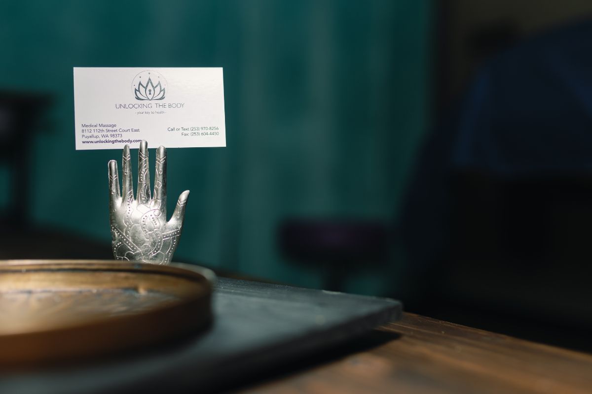 Unlocking the Body massage therapy business card on silver hand stand in tranquil spa setting, Puyallup wellness brand.