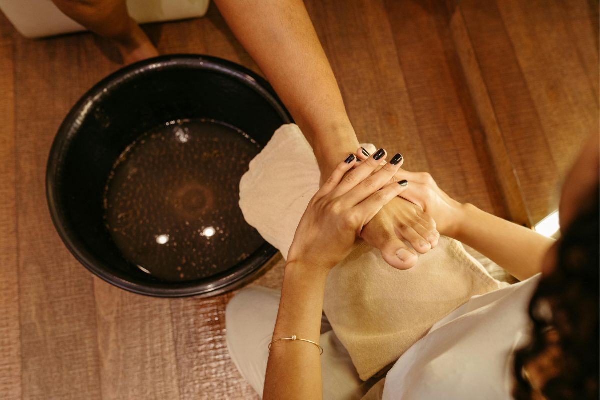 Therapist giving spa foot massage by soak bowl, client’s foot on towel, relaxing pedicure treatment