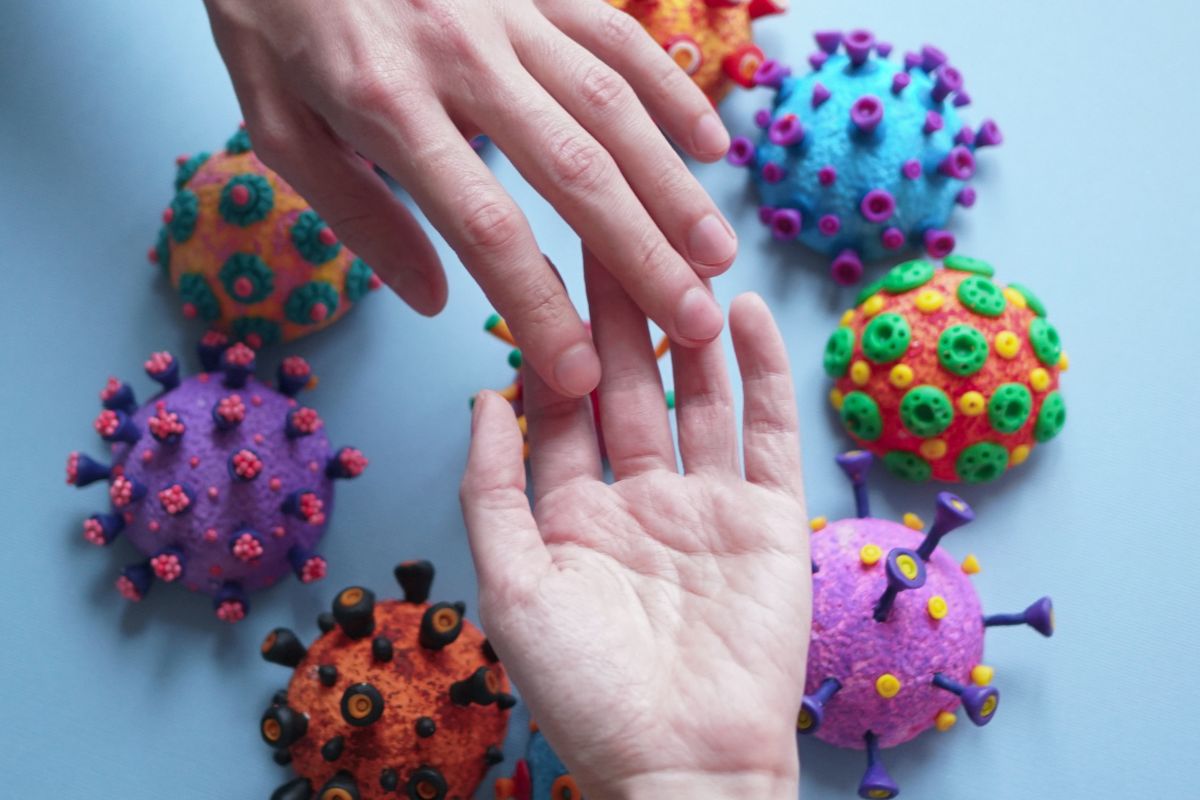 Hands touching among colorful coronavirus models symbolizing COVID-19 transmission and hygiene awareness.