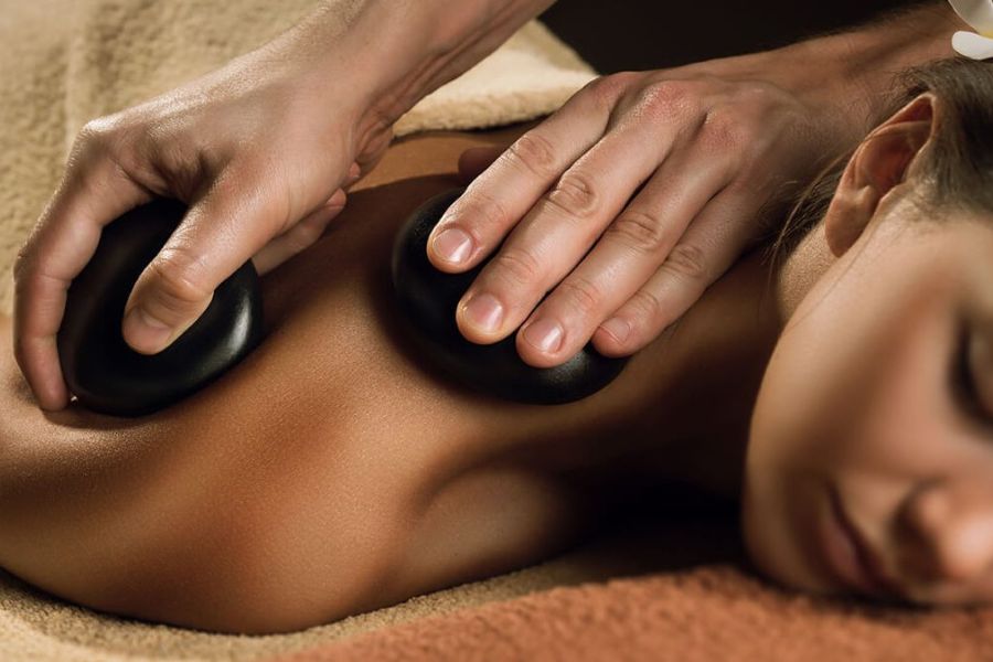 Hot stone massage on person's shoulder at spa, relaxing back therapy for muscle tension relief and wellness treatment.