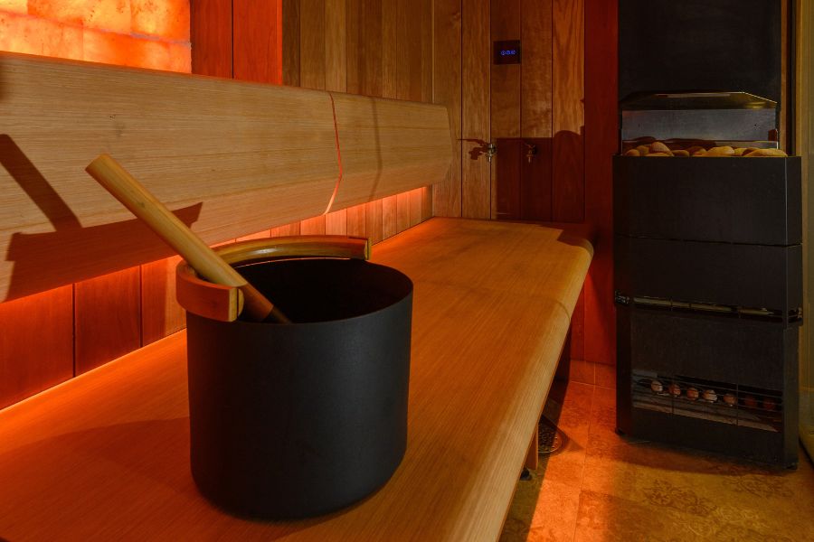 Luxury spa sauna interior with wooden bench, bucket and ladle, and hot stone heater, warm ambient lighting for relaxation.