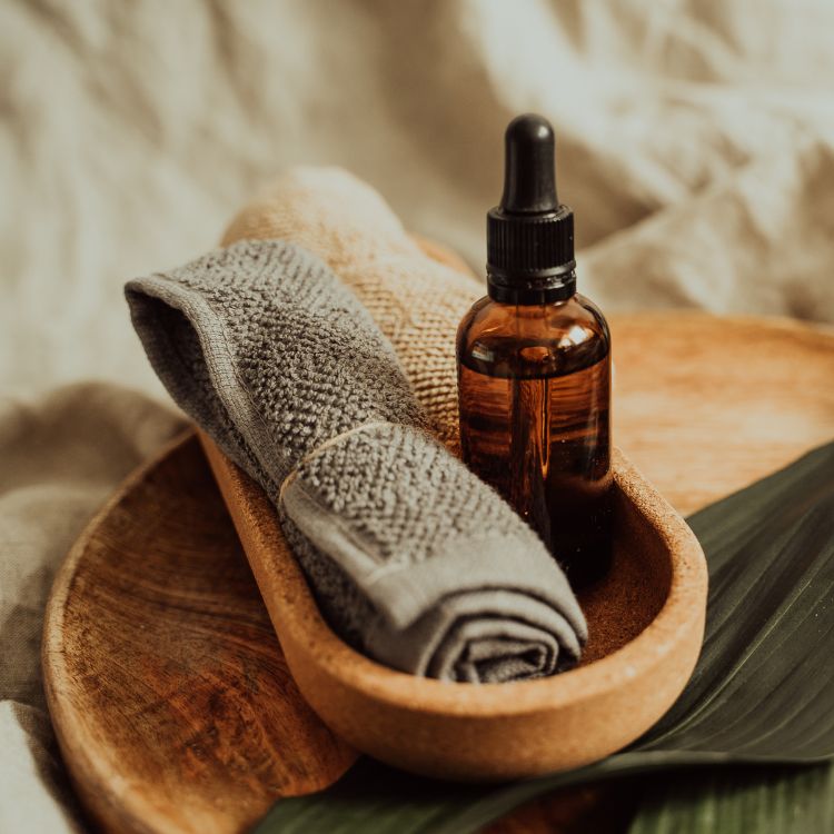Amber dropper bottle of essential oil with rolled towels in wooden tray, natural spa skincare aesthetic, minimalist decor