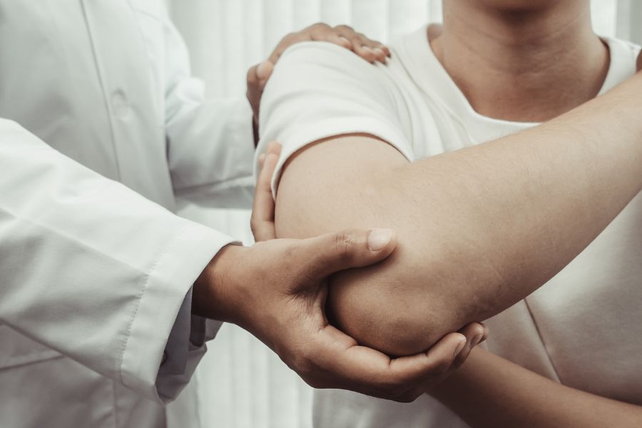 Physical therapist evaluating patient's elbow pain during orthopedic exam and arm rehabilitation