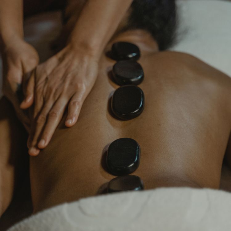 Hot stone massage therapy at spa, basalt stones on back with therapist’s hands relieving tension and stress.
